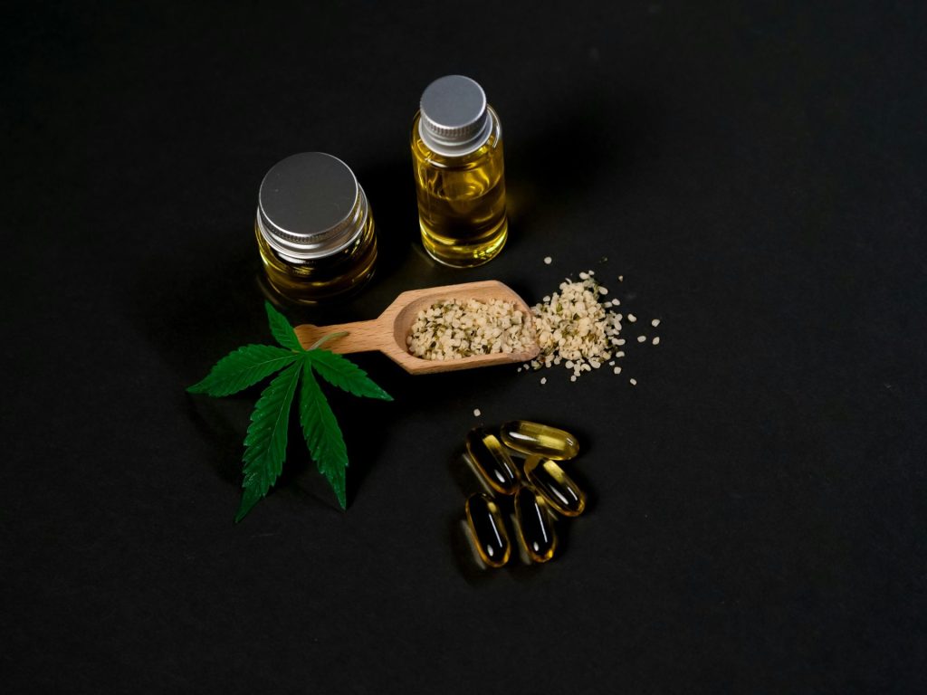 High-quality cannabis oil and capsules with hemp seeds and leaf on a dark backdrop.